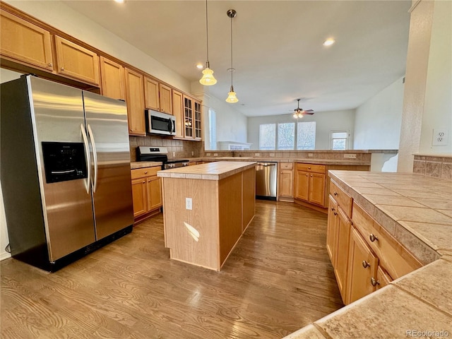 kitchen featuring a kitchen island, appliances with stainless steel finishes, light wood-type flooring, tile counters, and glass insert cabinets