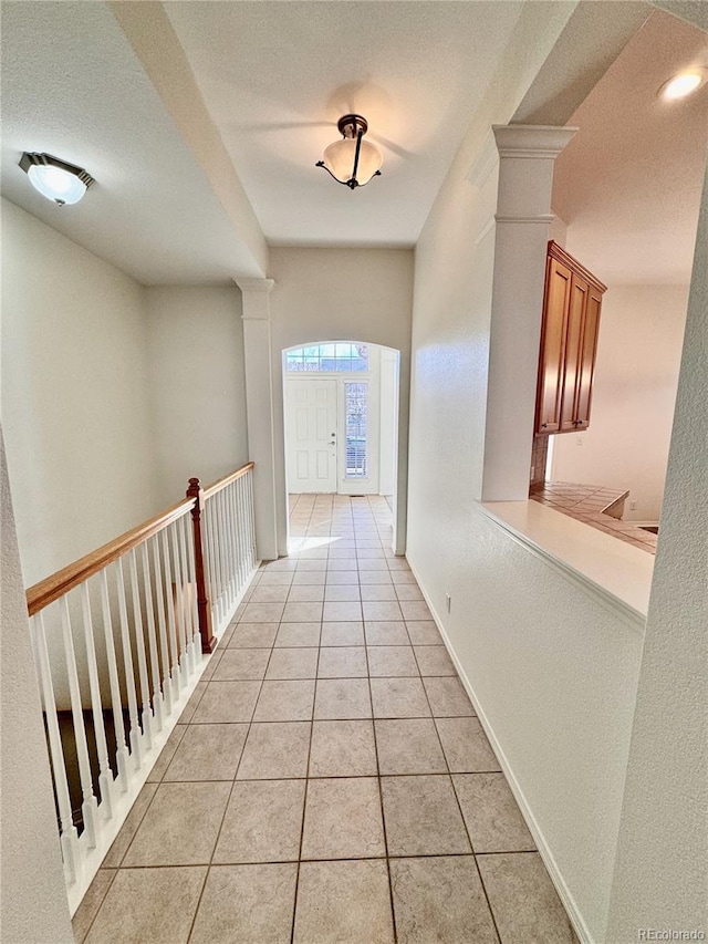 hall featuring light tile patterned floors, a textured ceiling, decorative columns, and baseboards