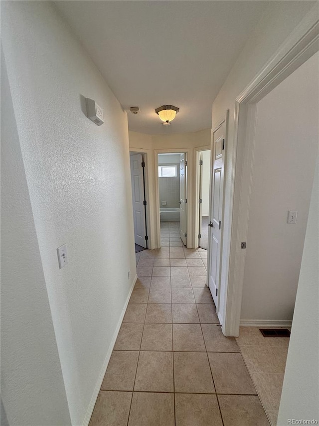 corridor featuring visible vents, baseboards, and light tile patterned floors