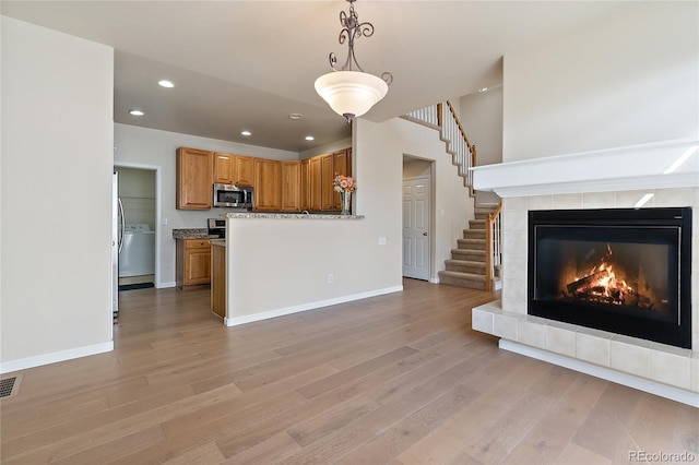 kitchen with light wood-type flooring, light stone counters, a tile fireplace, washer / dryer, and hanging light fixtures