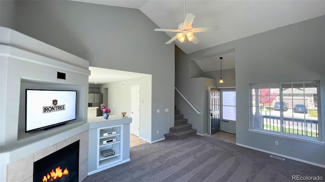 unfurnished living room with ceiling fan, high vaulted ceiling, carpet, a tile fireplace, and stairway