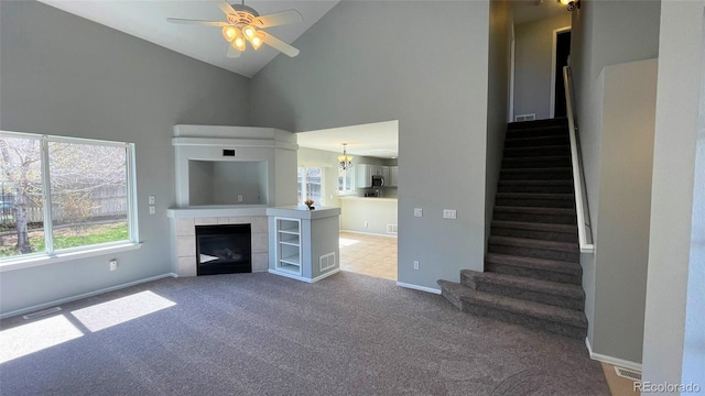 unfurnished living room with ceiling fan, high vaulted ceiling, carpet, a tile fireplace, and stairway