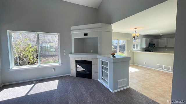 unfurnished living room with high vaulted ceiling, a notable chandelier, a tile fireplace, and visible vents