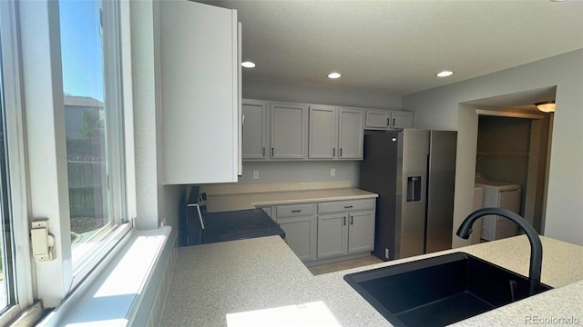 kitchen featuring stainless steel refrigerator with ice dispenser, light countertops, black electric range, a sink, and independent washer and dryer