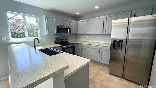 kitchen with appliances with stainless steel finishes, a sink, light countertops, a peninsula, and recessed lighting