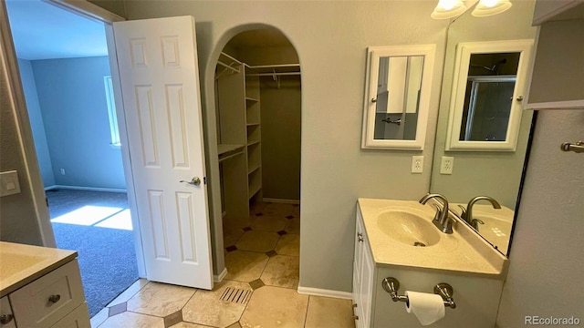 bathroom featuring baseboards, tile patterned floors, a walk in closet, and vanity