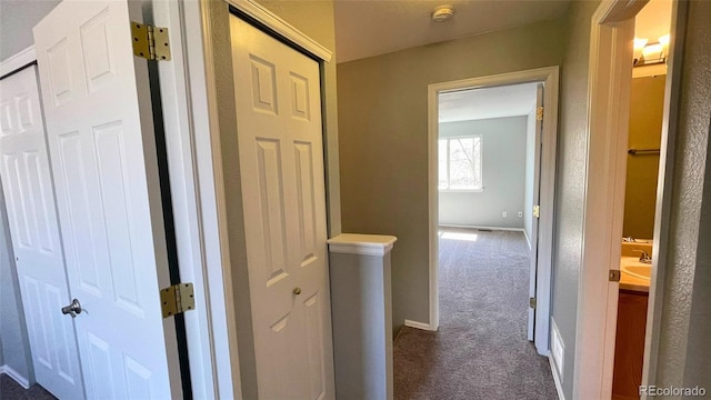hall featuring baseboards, an upstairs landing, and dark colored carpet