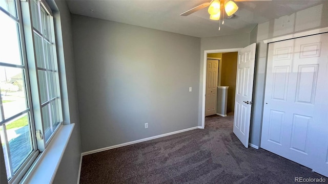 unfurnished bedroom with a closet, baseboards, multiple windows, and dark colored carpet