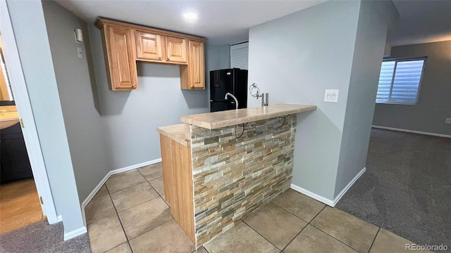 kitchen featuring light countertops, baseboards, tile patterned floors, freestanding refrigerator, and a peninsula