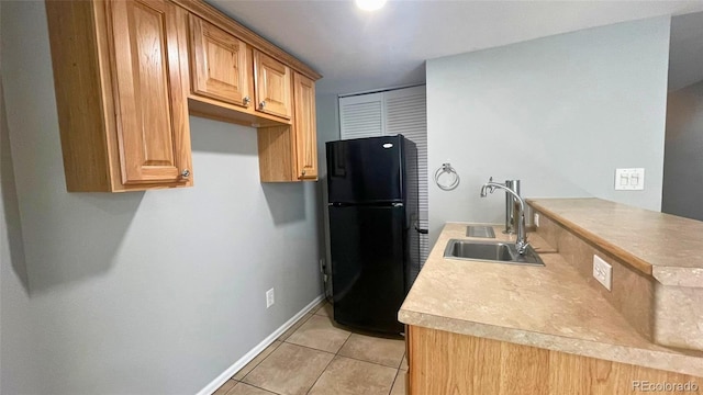 kitchen featuring light tile patterned flooring, a sink, light countertops, freestanding refrigerator, and a peninsula
