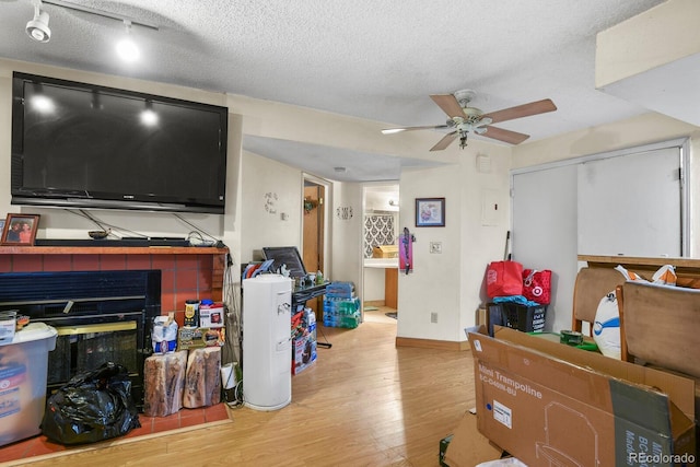 living area with ceiling fan, a textured ceiling, baseboards, and wood finished floors