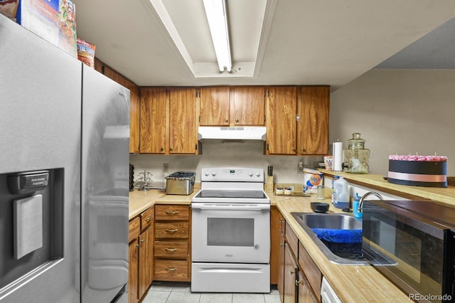 kitchen with light tile patterned floors, brown cabinetry, appliances with stainless steel finishes, light countertops, and under cabinet range hood