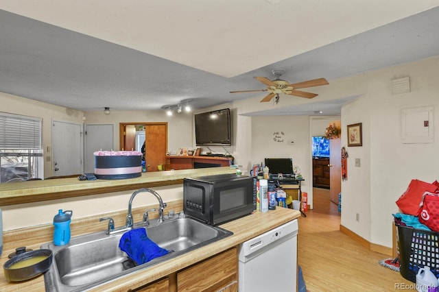 kitchen featuring white dishwasher, light countertops, light wood-style floors, black microwave, and a sink