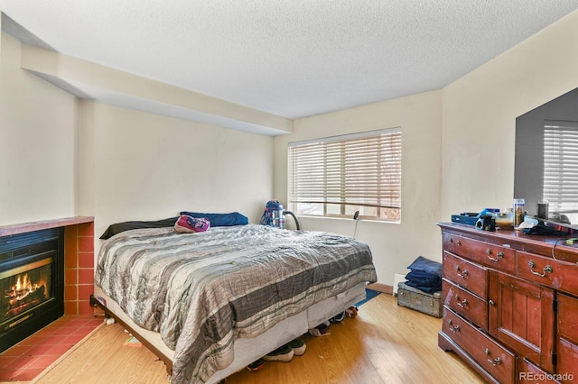 bedroom featuring a textured ceiling, light wood finished floors, multiple windows, and a fireplace