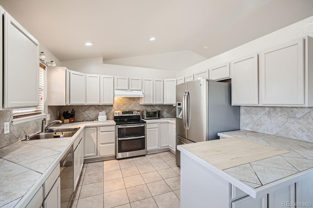 kitchen featuring kitchen peninsula, stainless steel appliances, vaulted ceiling, and white cabinetry