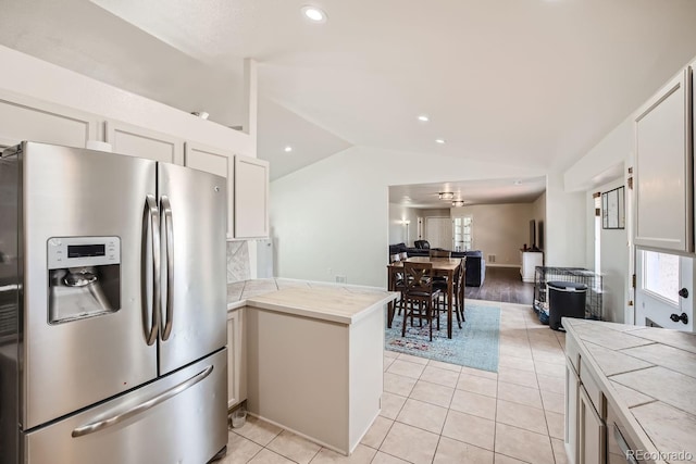 kitchen with white cabinets, vaulted ceiling, light tile patterned floors, kitchen peninsula, and stainless steel fridge