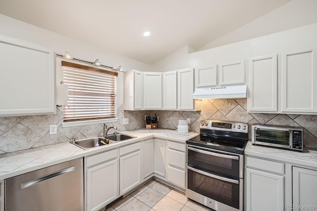 kitchen with appliances with stainless steel finishes, white cabinets, vaulted ceiling, and sink