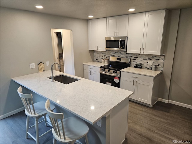 kitchen with appliances with stainless steel finishes, dark wood finished floors, a breakfast bar, backsplash, and white cabinets