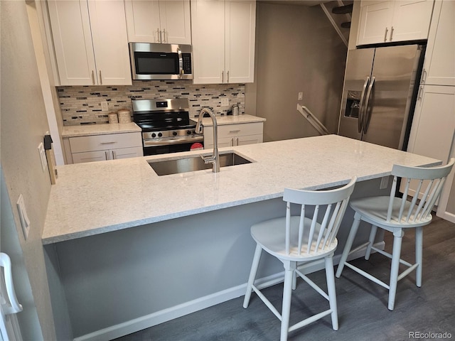 kitchen with appliances with stainless steel finishes, tasteful backsplash, dark wood finished floors, light stone counters, and a kitchen breakfast bar