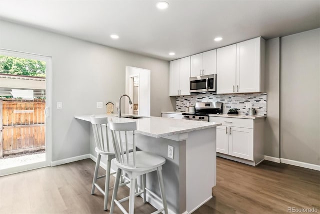 1927 S Peoria St, Aurora, CO 80014 - kitchen featuring stainless steel appliances, a kitchen breakfast bar, dark wood-style flooring, decorative backsplash, and recessed lighting