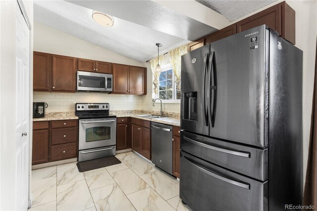 kitchen featuring pendant lighting, lofted ceiling, backsplash, sink, and appliances with stainless steel finishes