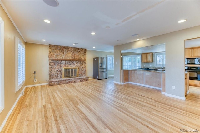 unfurnished living room with baseboards, light wood-type flooring, ornamental molding, a stone fireplace, and recessed lighting