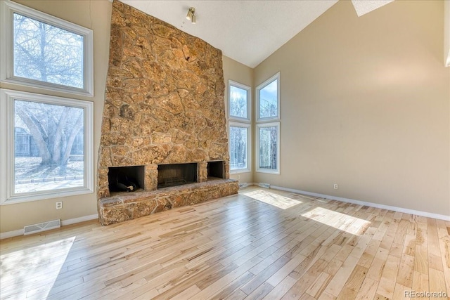 unfurnished living room featuring wood finished floors, baseboards, visible vents, high vaulted ceiling, and a stone fireplace