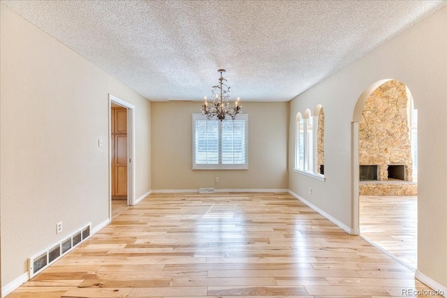 unfurnished dining area with visible vents, baseboards, light wood-style floors, a notable chandelier, and a textured ceiling