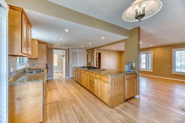 kitchen with a sink, light wood-type flooring, light stone counters, and baseboards