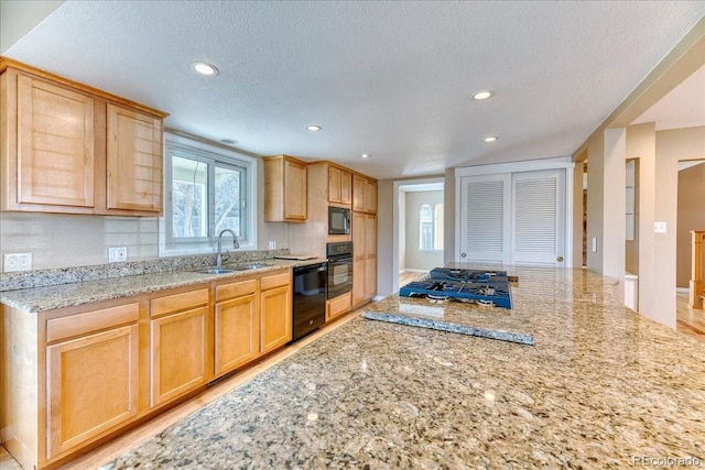 kitchen with black appliances, light brown cabinetry, a sink, light stone counters, and a textured ceiling