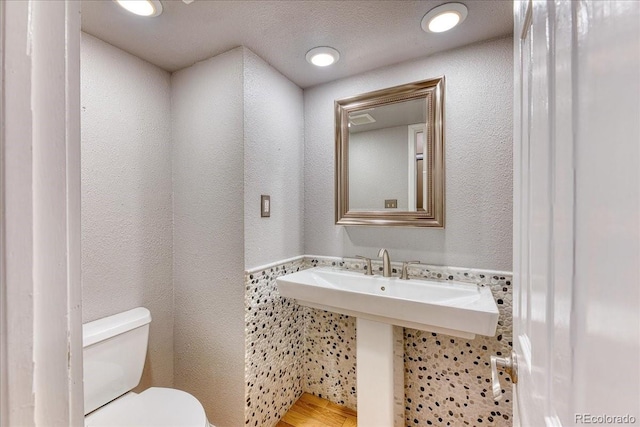 half bath with toilet, a textured wall, and recessed lighting