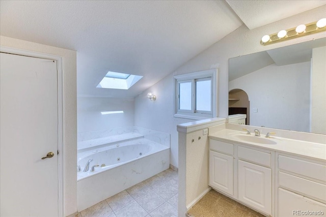 full bath featuring vanity, vaulted ceiling with skylight, tile patterned floors, a tub with jets, and a textured ceiling