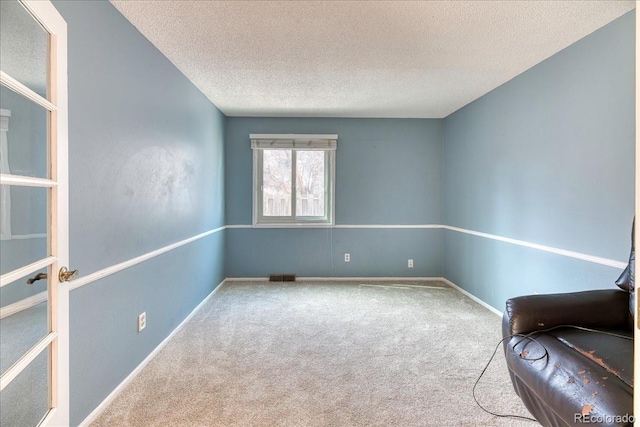 unfurnished room with visible vents, baseboards, carpet, and a textured ceiling