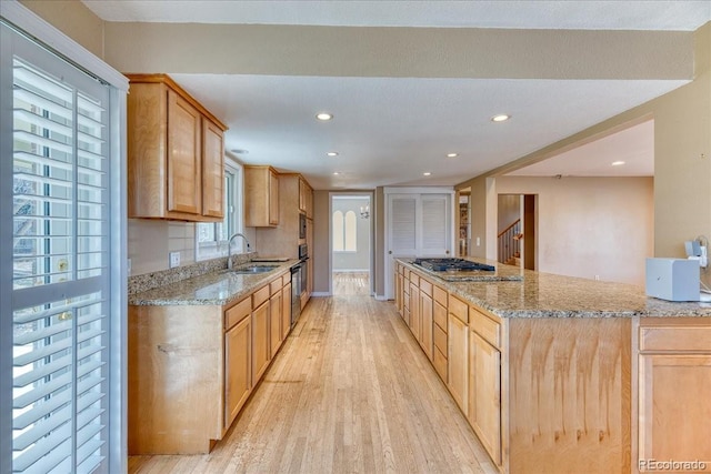 kitchen featuring a sink, light wood finished floors, gas stovetop, light stone counters, and recessed lighting