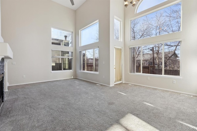 unfurnished living room featuring a fireplace, a high ceiling, carpet flooring, a chandelier, and baseboards