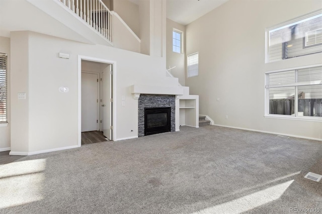 unfurnished living room featuring carpet, visible vents, a towering ceiling, a stone fireplace, and baseboards