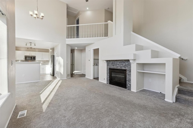 unfurnished living room with visible vents, stairway, a glass covered fireplace, light carpet, and a chandelier