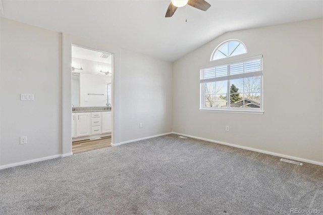 unfurnished bedroom featuring lofted ceiling, light colored carpet, visible vents, connected bathroom, and baseboards