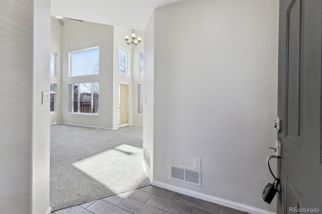 hall featuring a high ceiling, carpet flooring, visible vents, baseboards, and an inviting chandelier