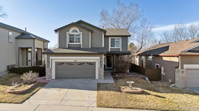 traditional home with a shingled roof, fence, a garage, stone siding, and driveway