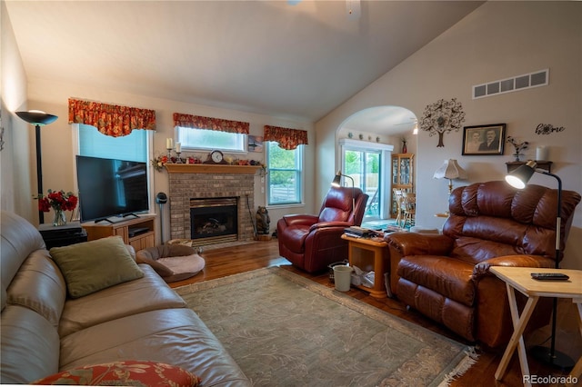 living area featuring wood finished floors, a brick fireplace, healthy amount of natural light, and vaulted ceiling