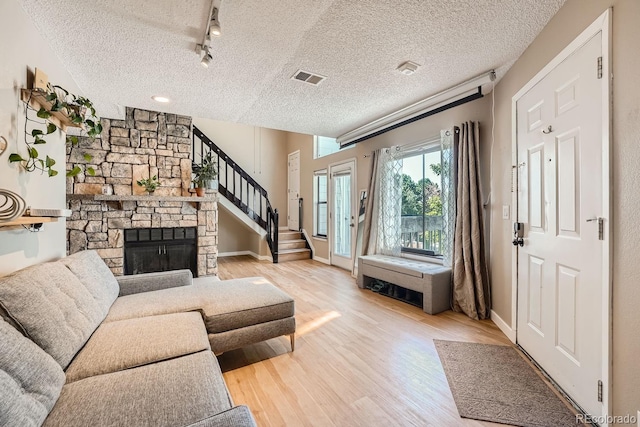 living room featuring a fireplace, track lighting, a textured ceiling, and light hardwood / wood-style floors