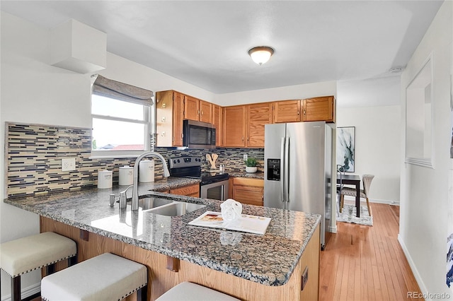 9946 Harrison St, Thornton, CO 80229 - kitchen featuring appliances with stainless steel finishes, a sink, a peninsula, decorative backsplash, and brown cabinetry