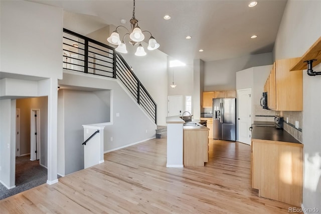 kitchen with light brown cabinets, stainless steel fridge with ice dispenser, a chandelier, light wood-type flooring, and a towering ceiling