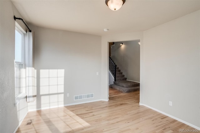 spare room with light wood-type flooring, visible vents, baseboards, and stairs