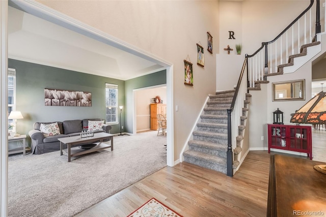 living room with crown molding, a high ceiling, and light wood-type flooring