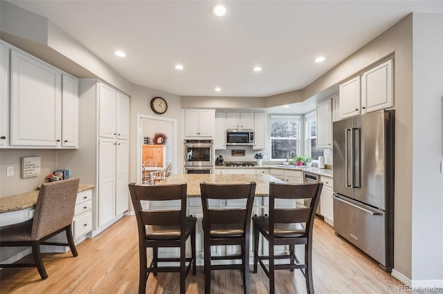 kitchen with white cabinets, a kitchen bar, a center island, stainless steel appliances, and light hardwood / wood-style flooring