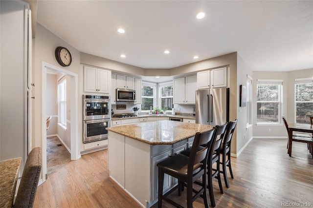 kitchen featuring appliances with stainless steel finishes, a kitchen breakfast bar, light stone counters, a kitchen island, and light wood-type flooring