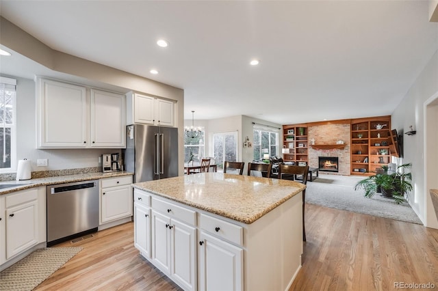 kitchen featuring decorative light fixtures, a kitchen island, stainless steel appliances, a fireplace, and white cabinets