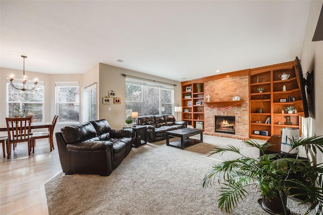 living room featuring an inviting chandelier, a fireplace, built in features, and light wood-type flooring